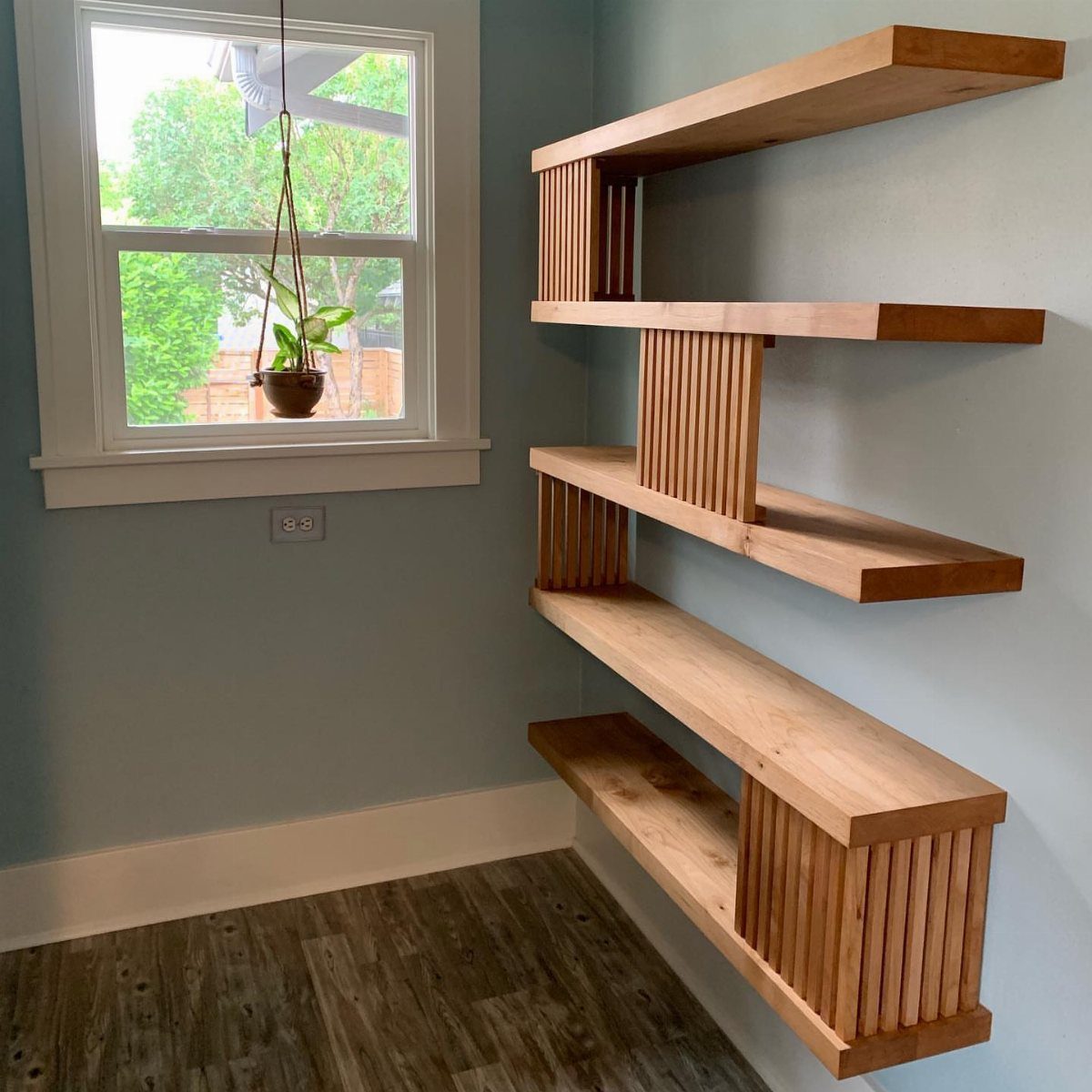 Light-brown wooden floating shelves with vertical slats mounted on a light blue wall.