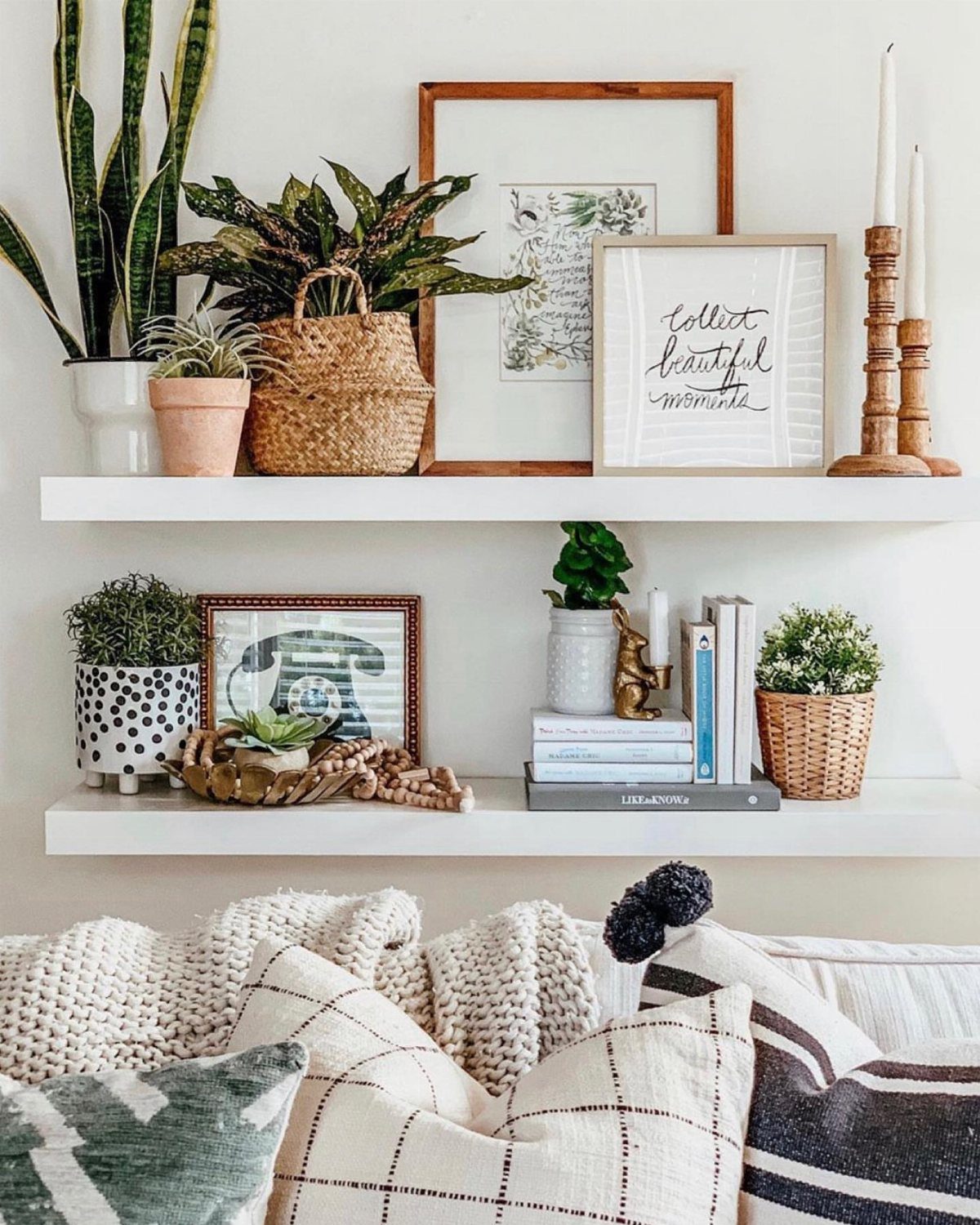 White floating shelves with plants and framed art above a cozy white sofa.