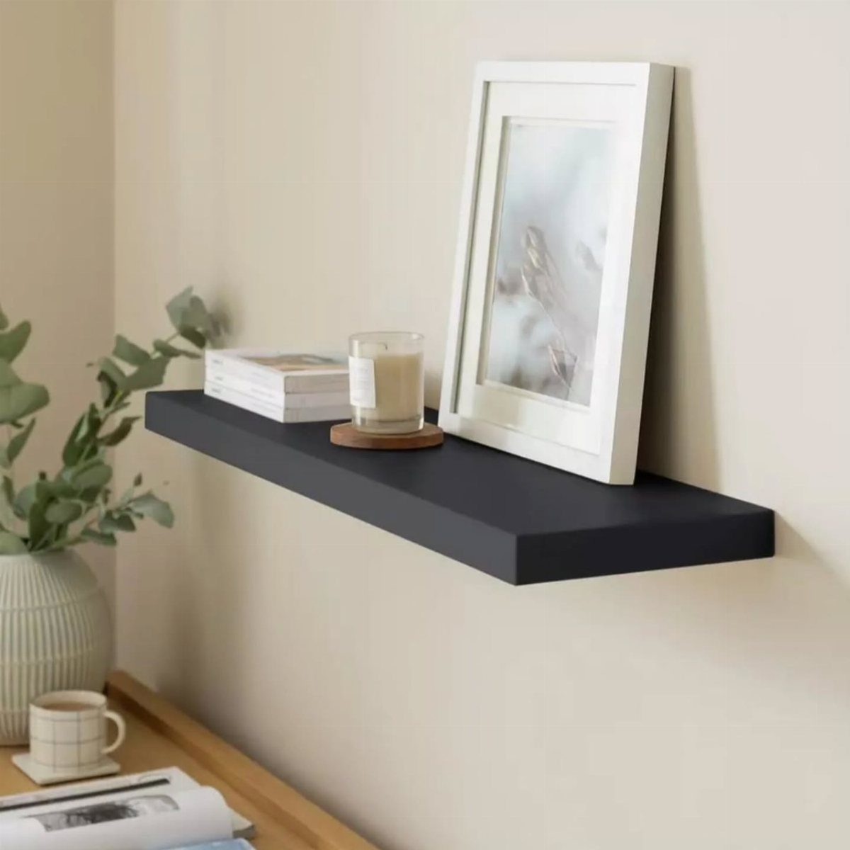 Black floating shelf on a beige wall holding a picture frame and candle.