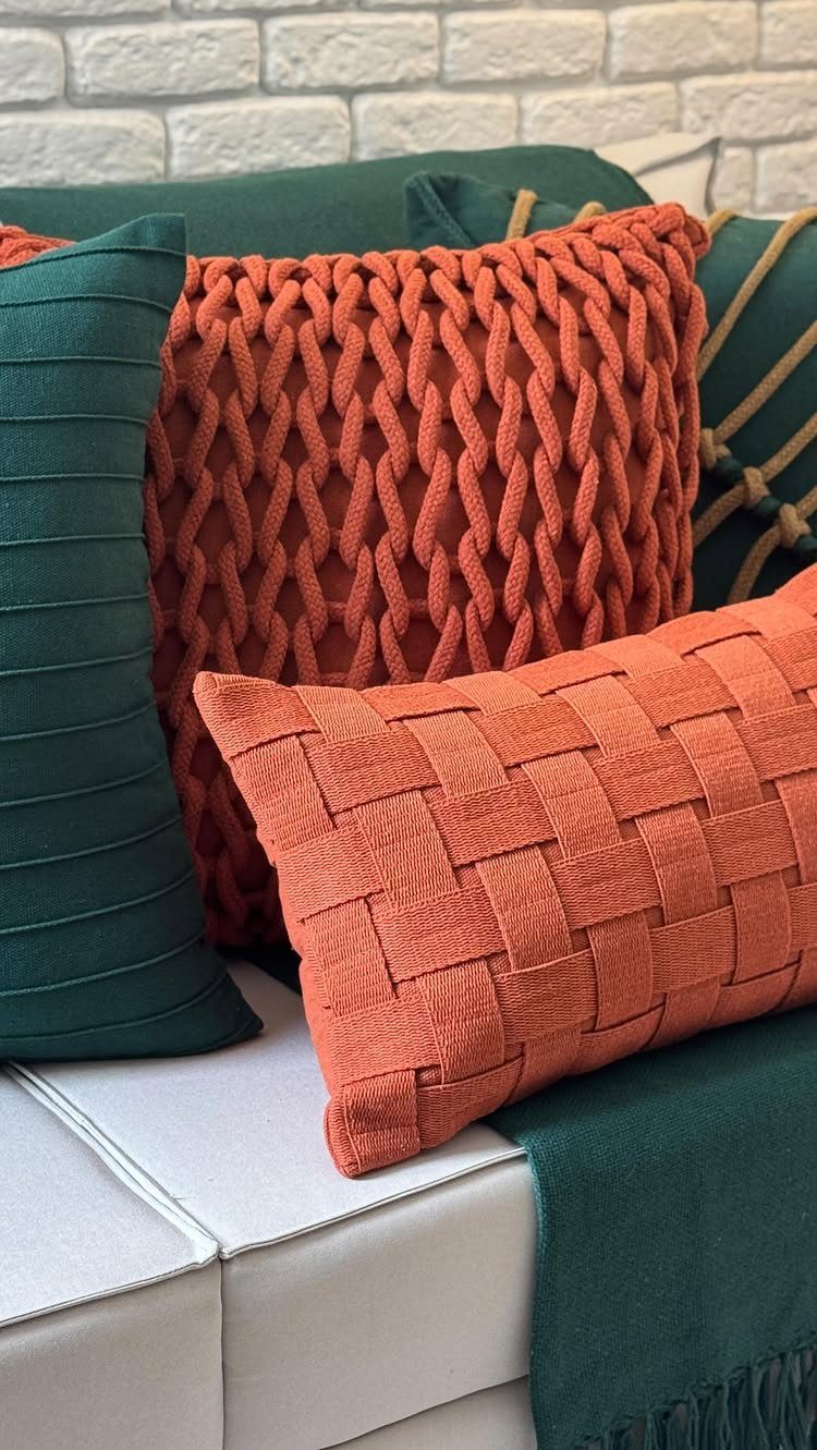 Orange and dark green textured pillows on a white sofa against brick wall