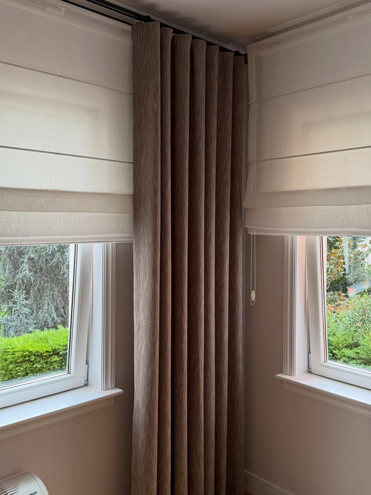 Brown pleated curtains and white Roman blinds installed on living room windows.