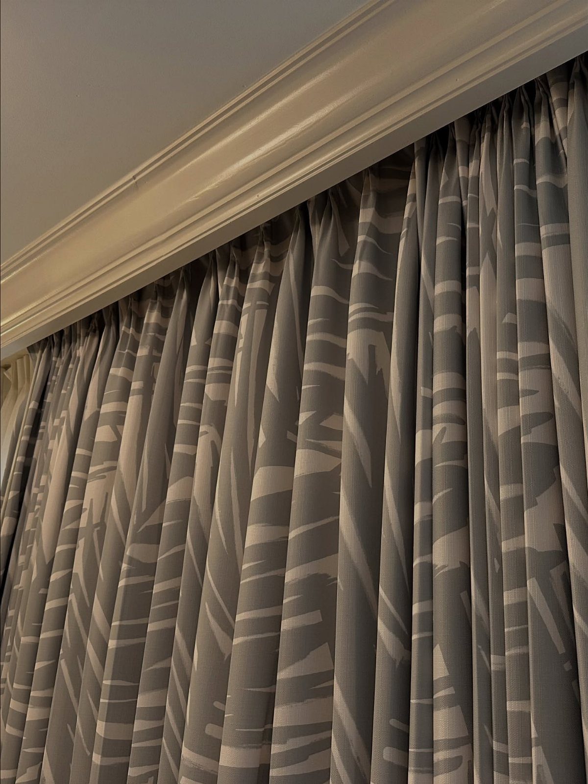 Grey patterned curtains hanging from a white ceiling molding in a room.