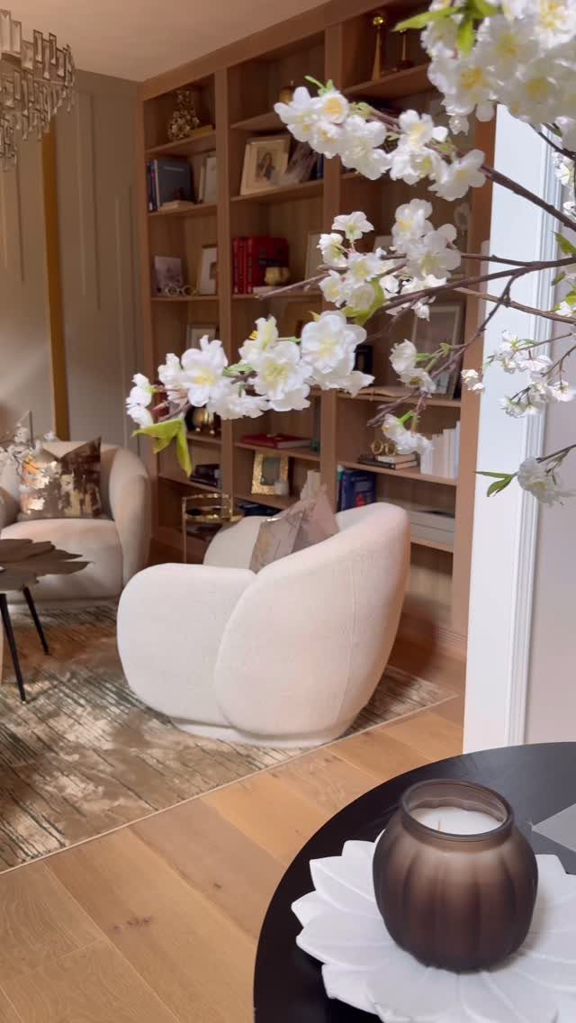 Built-in wooden bookshelves filled with books and decor behind curved white armchairs.
