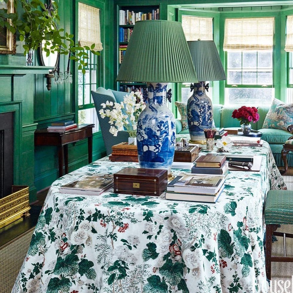 Floral tablecloth with blue and white porcelain lamps and decorative boxes in green room.