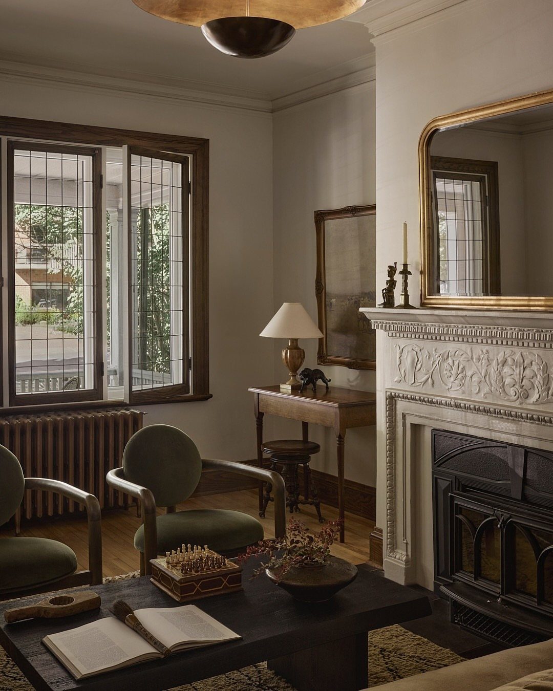 Elegant living room with a carved white fireplace, green velvet chairs, and gold mirror.