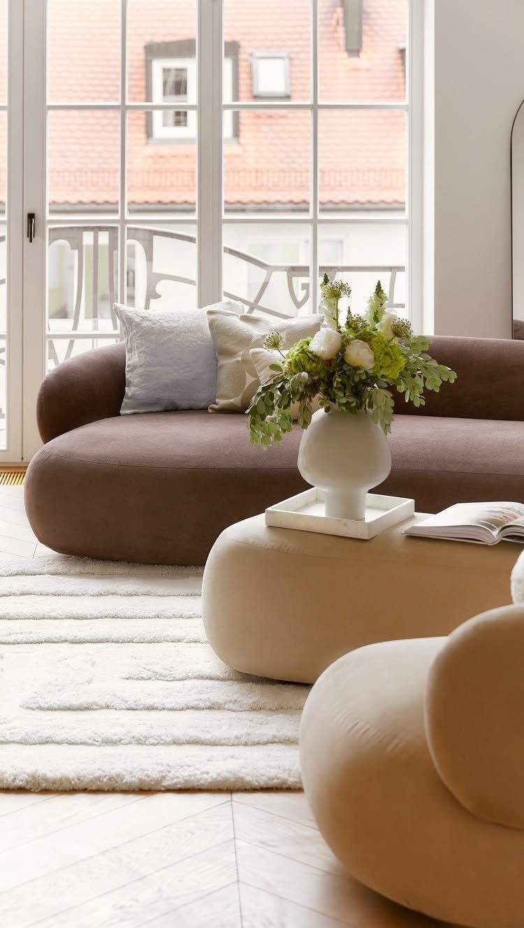 9 Living Room Couch Ideas for a Stylish Space 6 Brown curved sofa with white pillows and a rounded coffee table in a bright room.