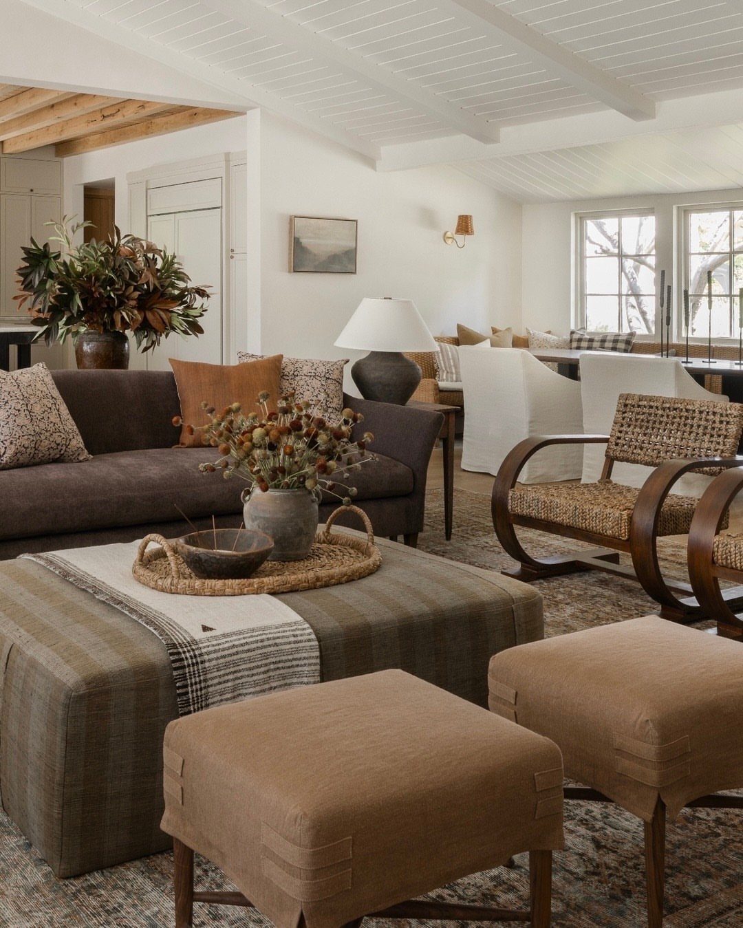 Large striped fabric ottoman coffee table with smaller tan ottomans in a living room.
