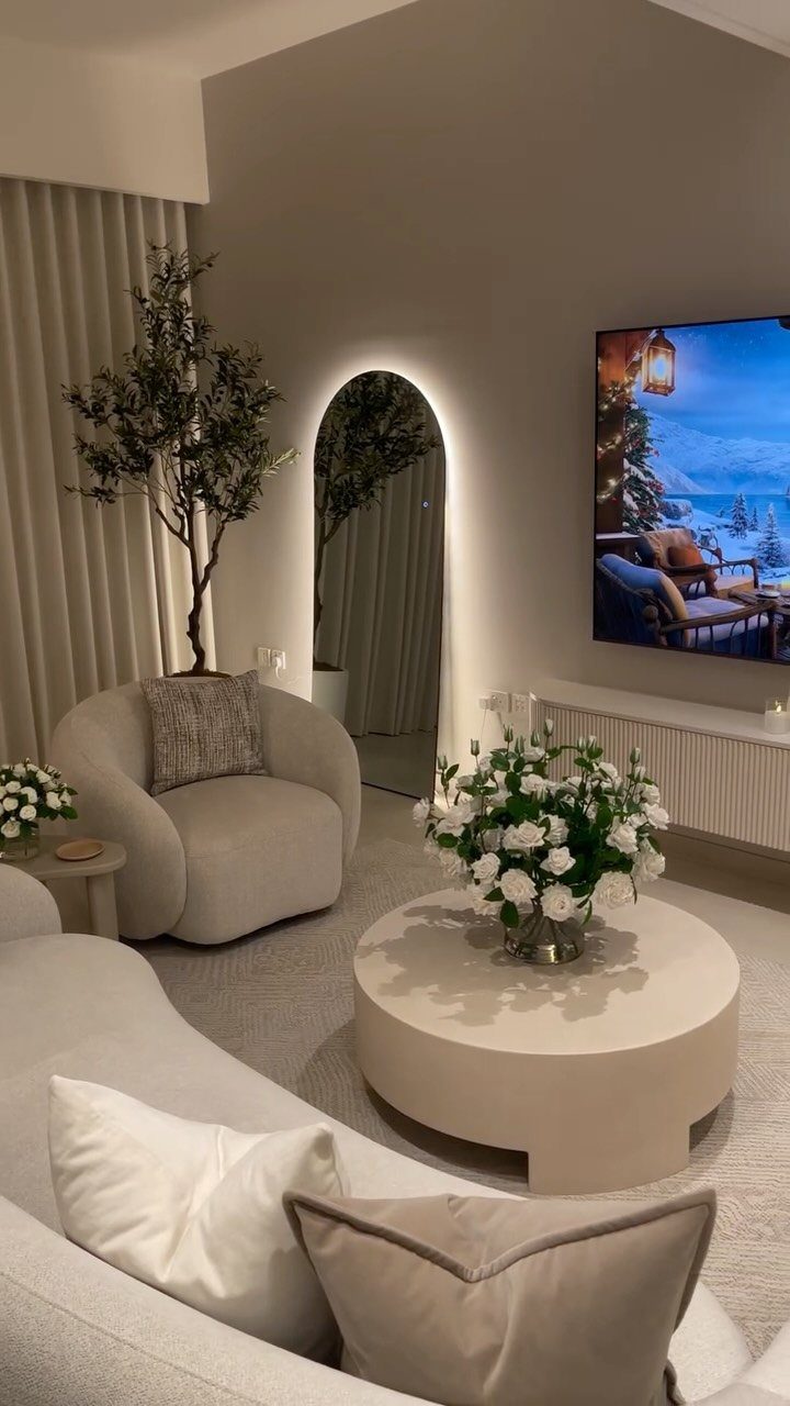 Modern neutral living room with curved white sofa, round coffee table, and white flowers.