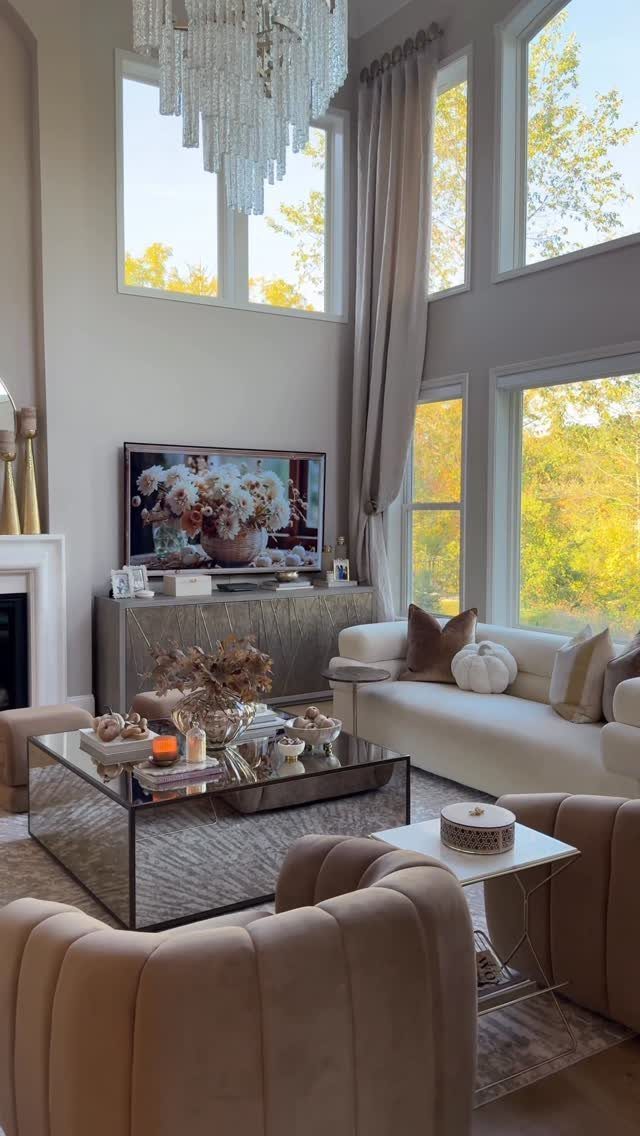 Living room with autumn-themed pillows and yellow fall foliage visible through large windows.