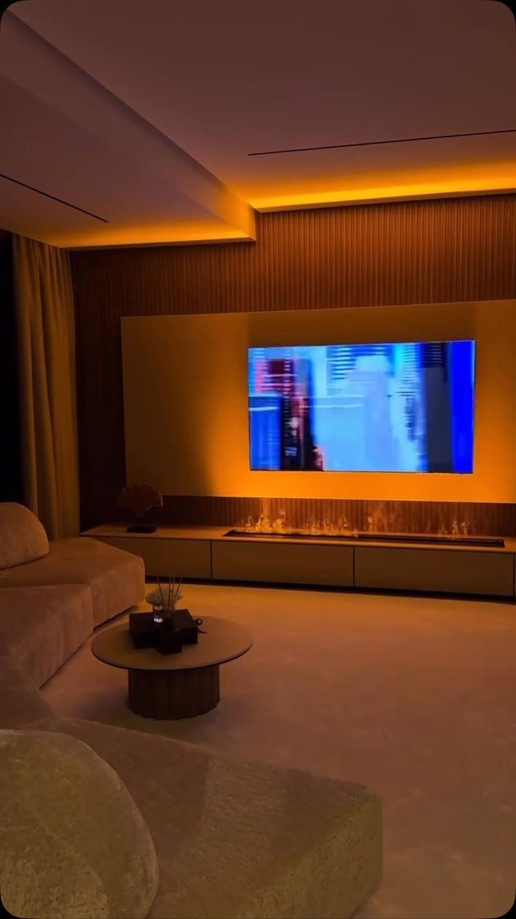 Modern living room with orange cove ceiling lighting, large TV, and linear fireplace.
