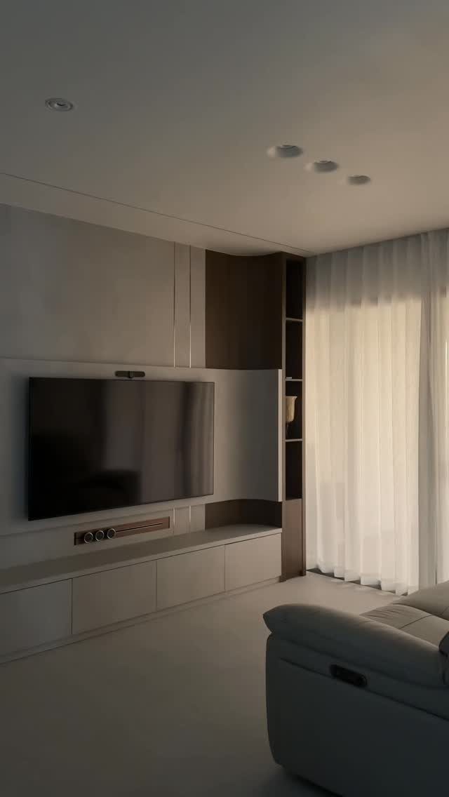 Modern living room with recessed ceiling lights, wall-mounted TV, and white cabinetry.