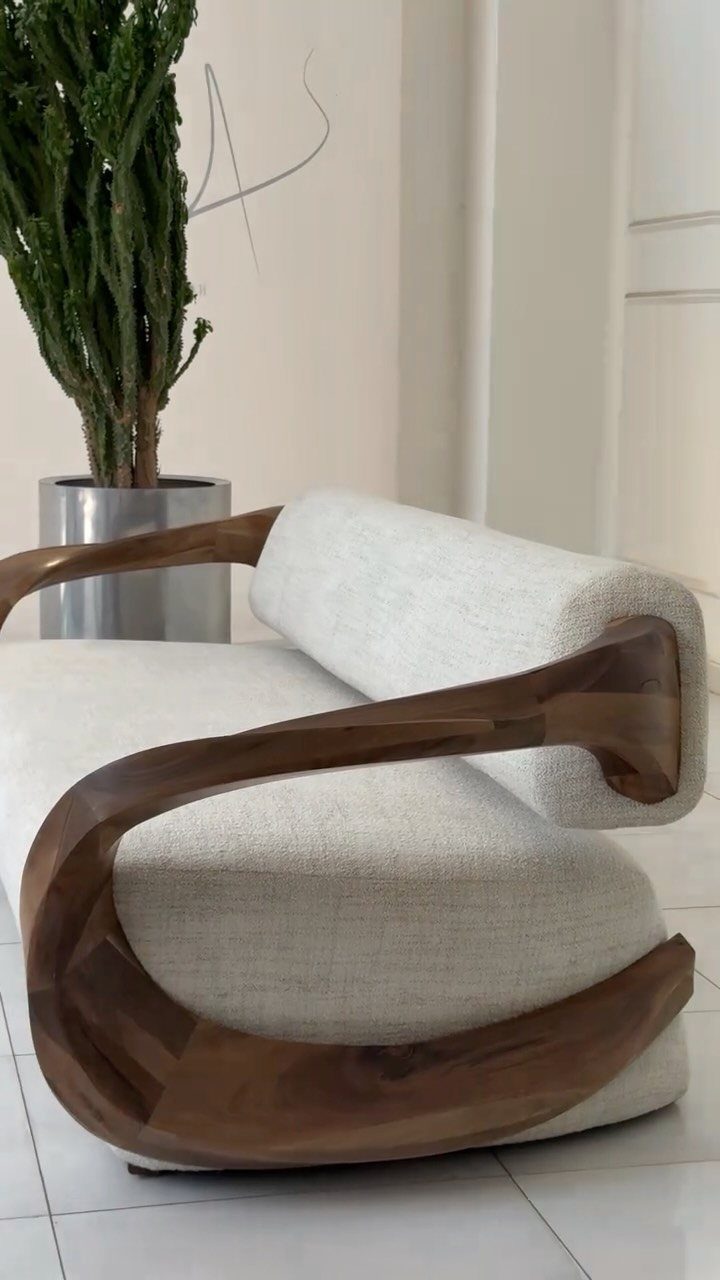 Modern armchair with curved wooden frame and white fabric next to a plant.