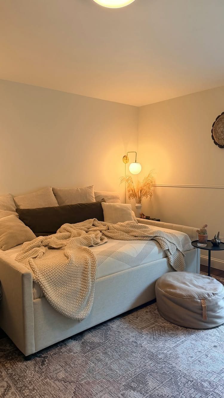 Light-colored daybed with knit throw and pillows on a grey patterned rug.