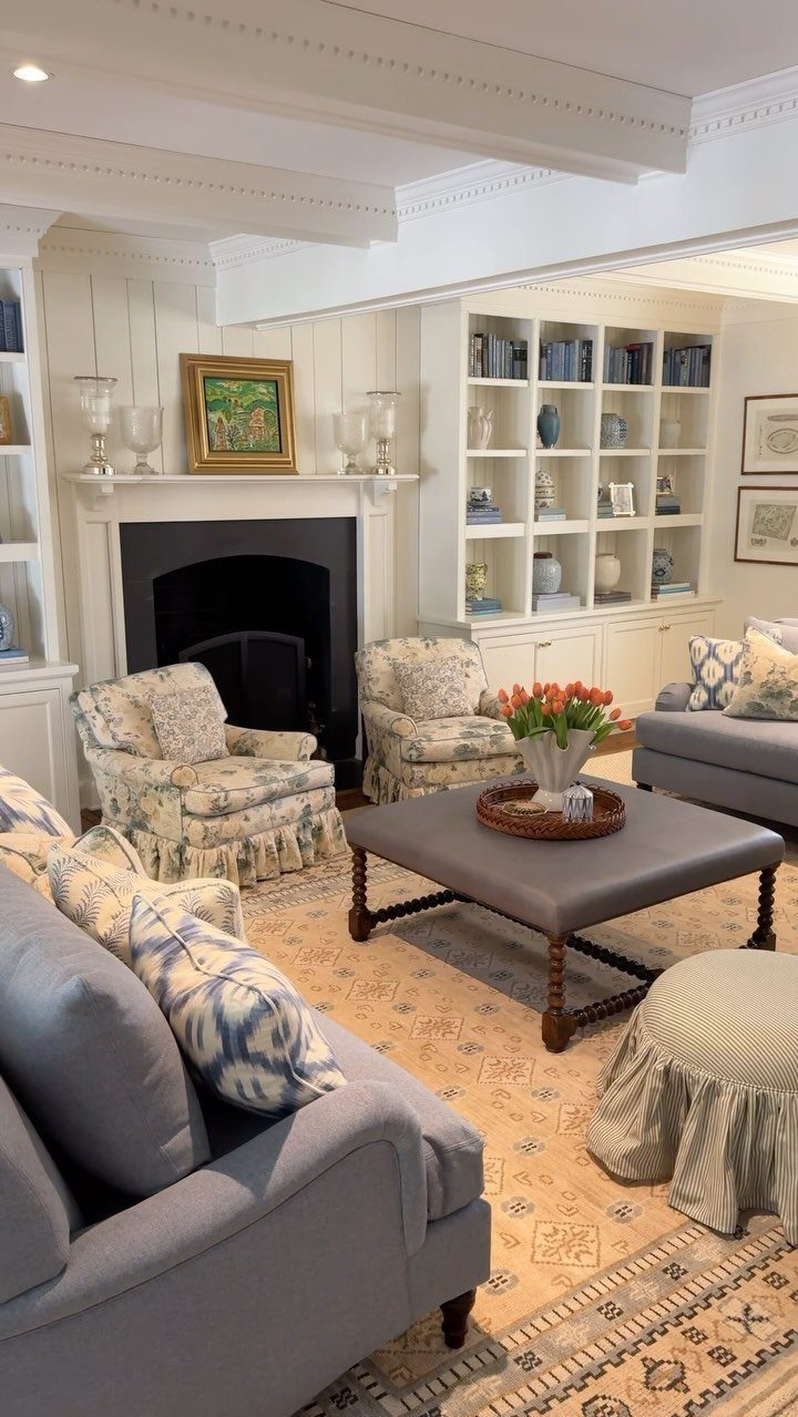 Grey upholstered square coffee table in a bright living room with floral armchairs.