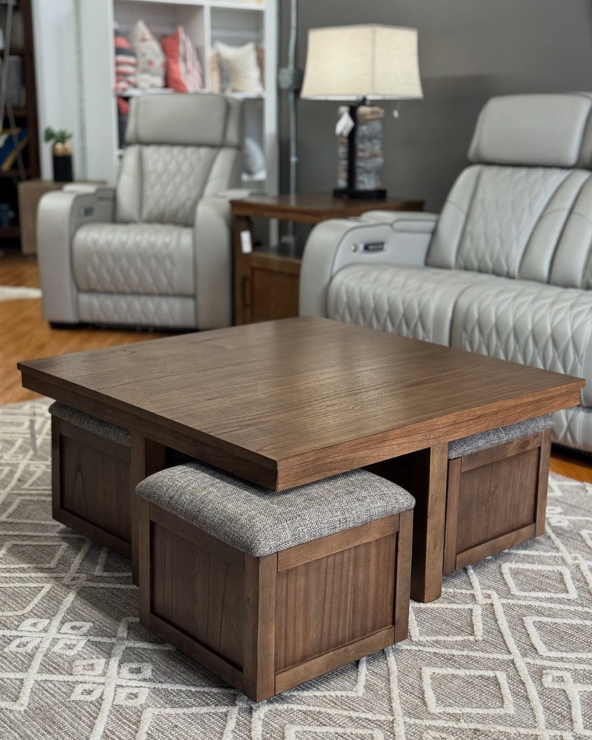 Brown wooden square coffee table with three grey fabric storage ottomans tucked underneath.