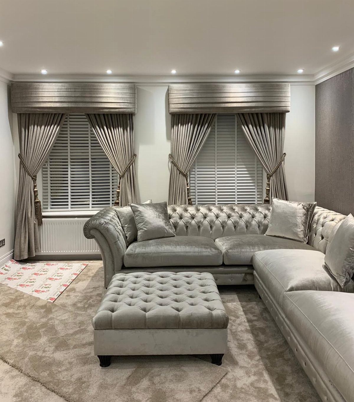 Grey pleated valances and curtains over windows in a living room with tufted furniture.