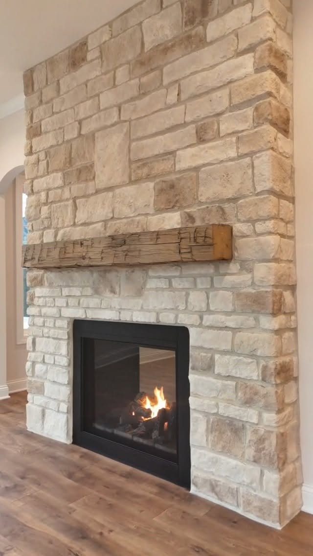 Stone fireplace with a rustic wooden mantel and burning fire on wood flooring