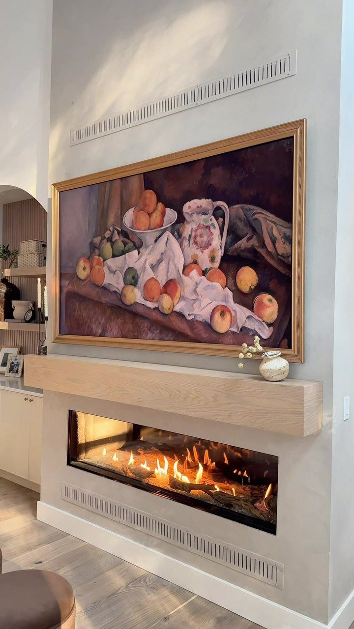 Linear built-in fireplace with a light wood mantel and a large still-life painting above.