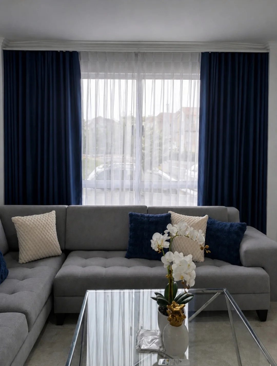 Navy blue curtains framing a window above a grey sectional sofa with pillows.