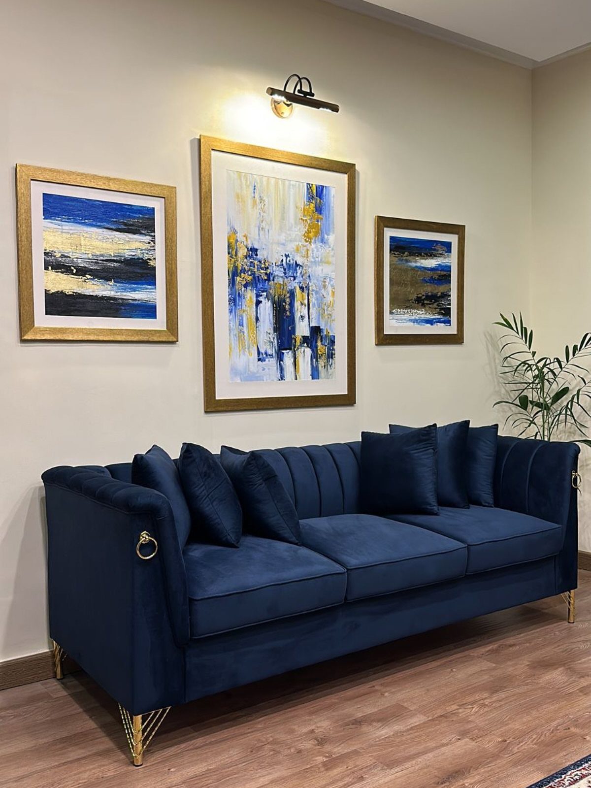 Navy blue velvet sofa with gold accents and abstract art on the wall