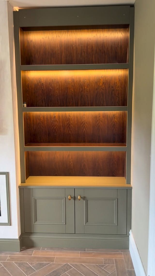Built-in sage green cabinets with illuminated wooden shelves and lower cupboard doors.