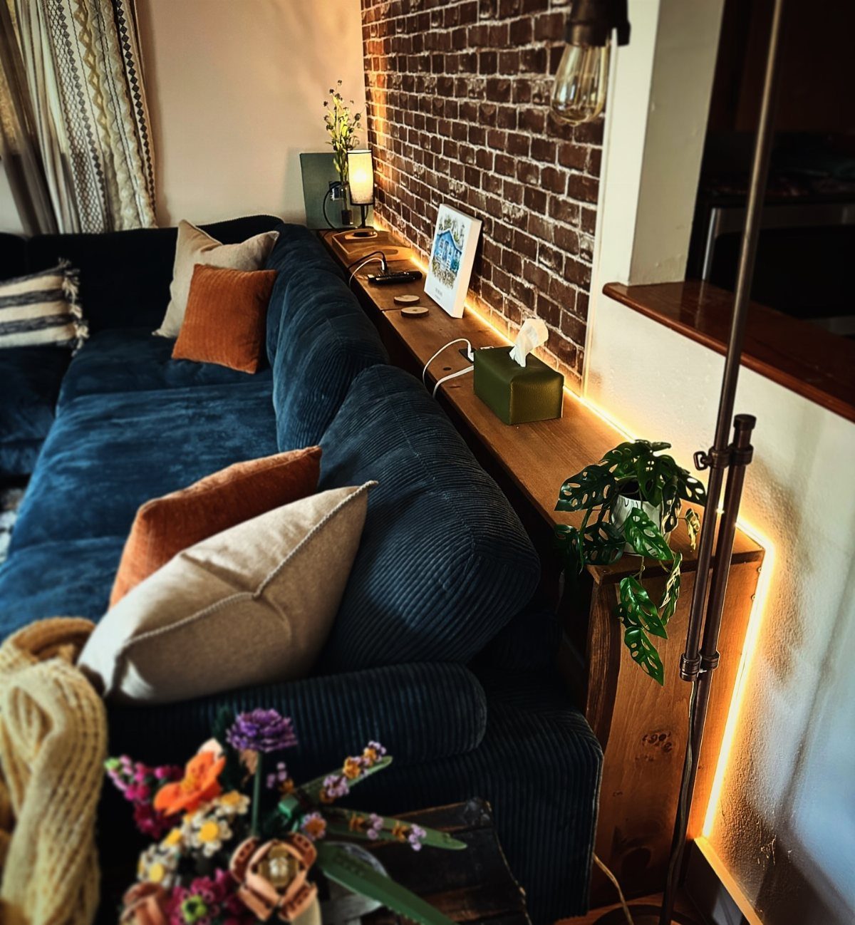 Wooden console table with warm lighting placed behind a dark blue corduroy sofa.
