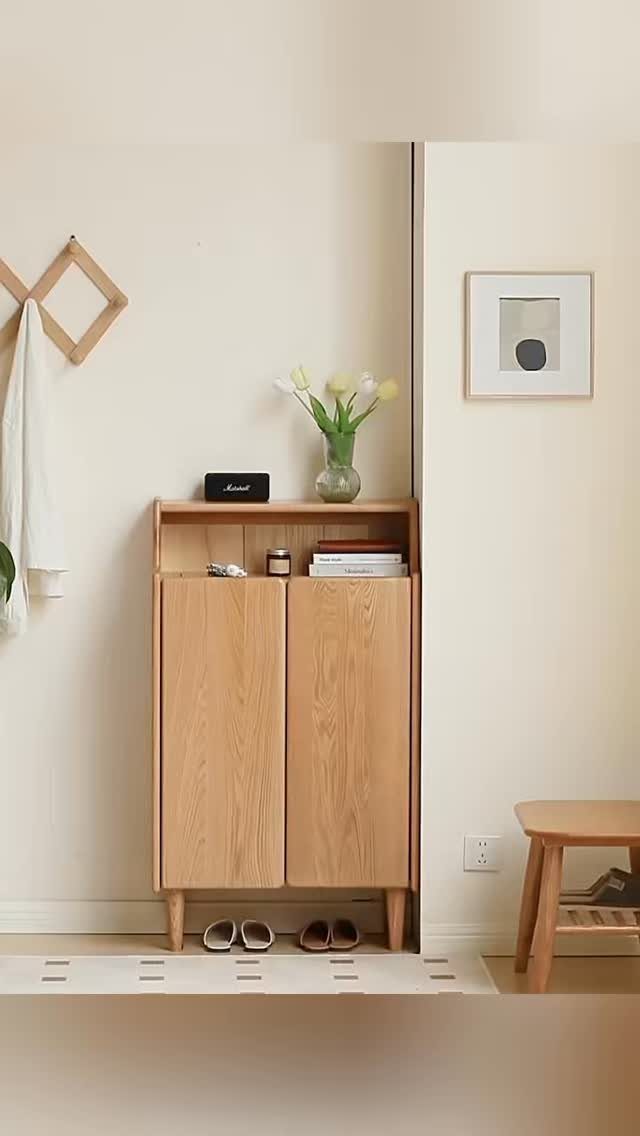 Slim light-wood storage cabinet with two doors and top shelf against a beige wall