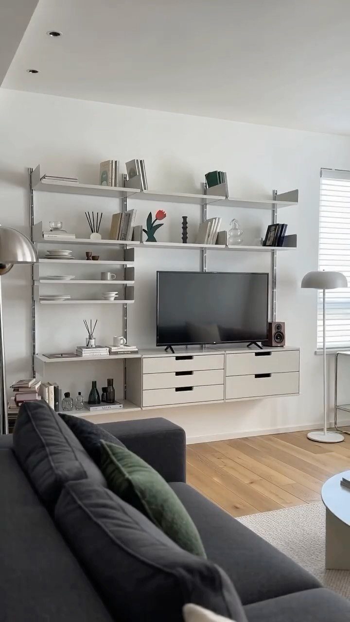 Wall-mounted shelving system with white shelves and drawers in a modern living room.