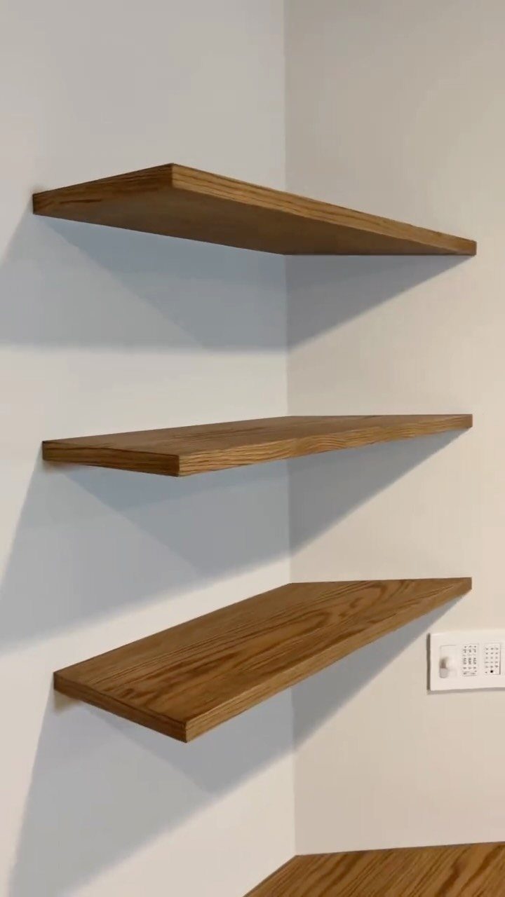 Floating wooden corner shelves installed on a clean white living room wall.