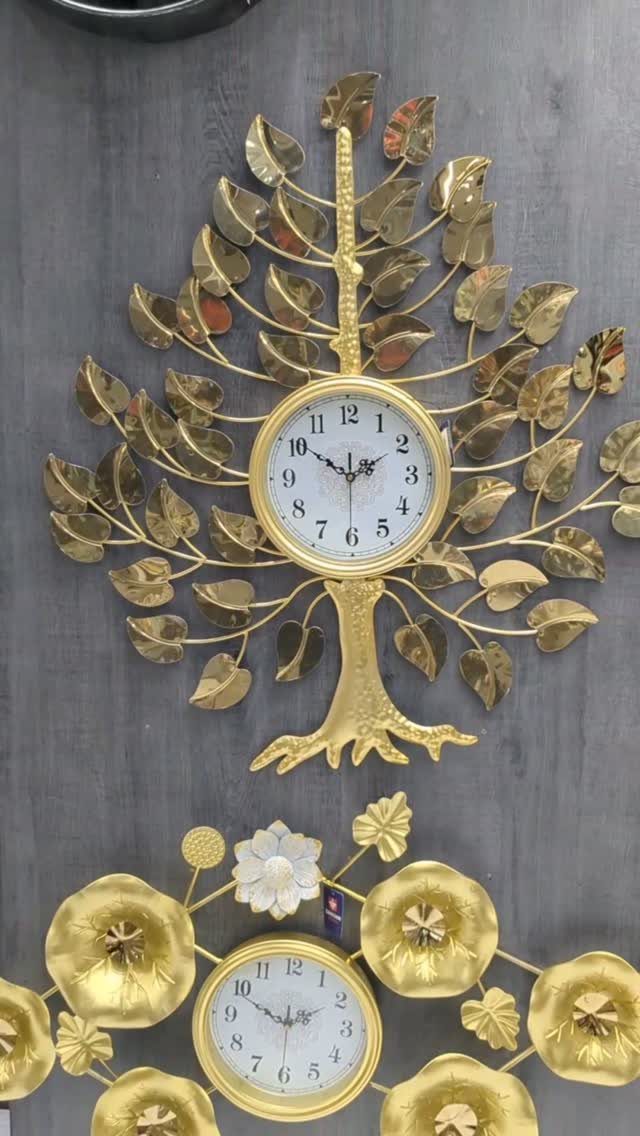 Two ornate gold wall clocks, one tree-shaped and one floral, on a grey wall.