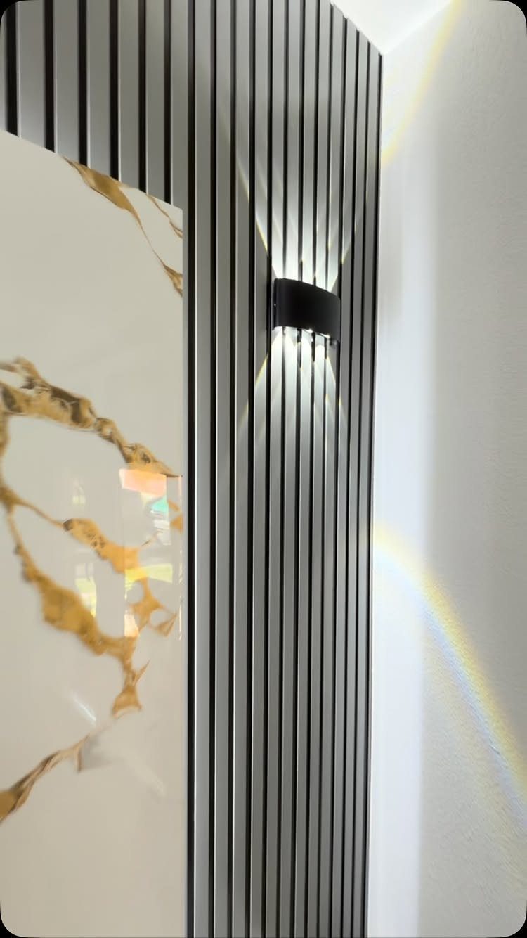 Modern wall design with grey vertical slats, gold-veined marble panel, and a black sconce.