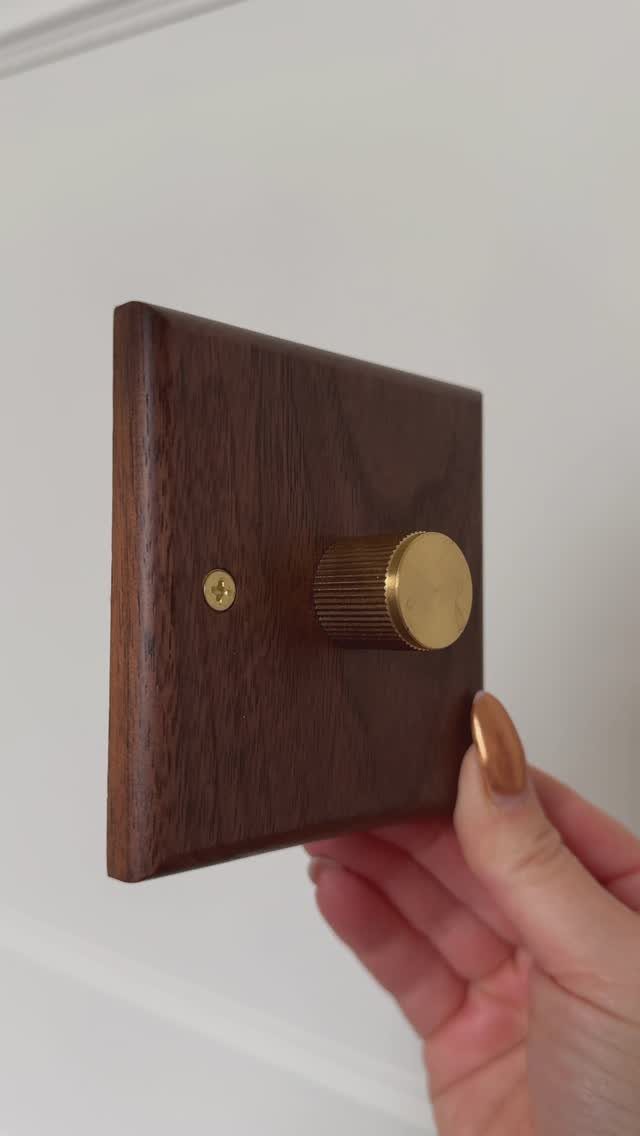 Wooden light switch plate with a brass rotary dimmer knob on white wall.