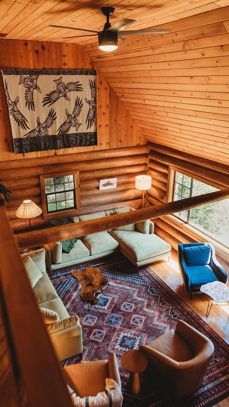 Rustic log cabin living room with warm lamps, green sectional, and patterned red rug.