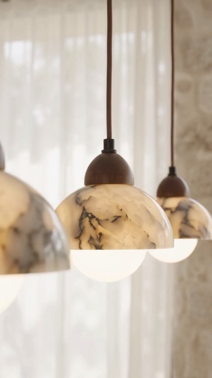 Three marbled glass pendant lights with wooden accents hanging against white sheer curtains.