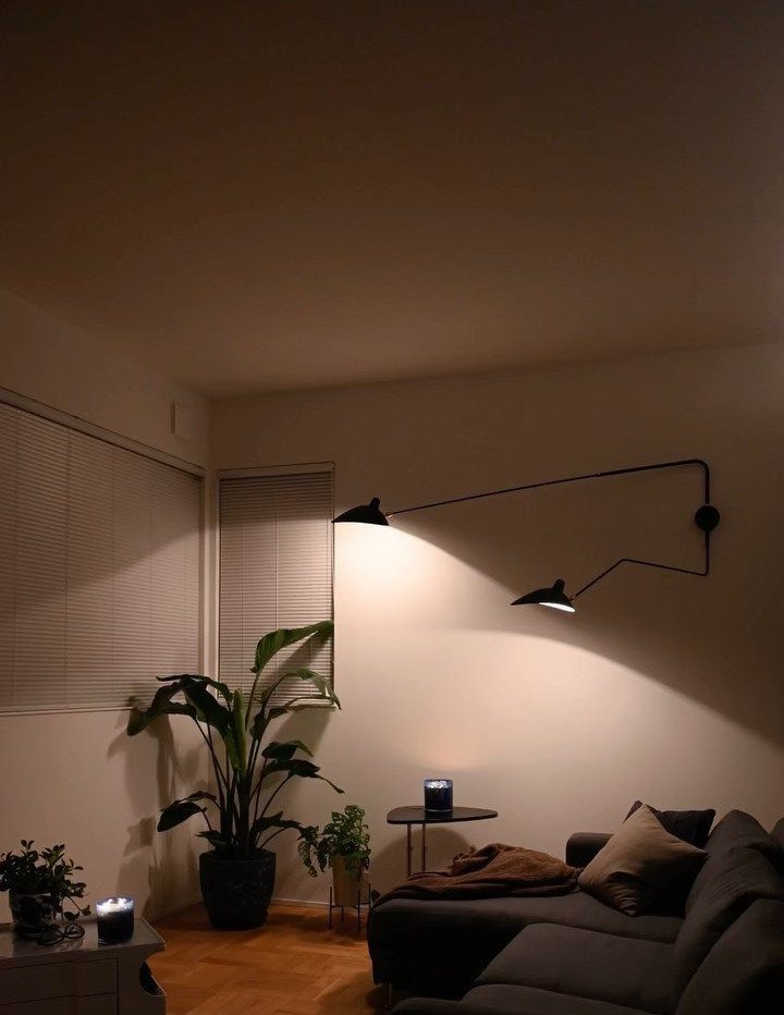 Black double-arm wall lamp casting warm light in a modern living room setting