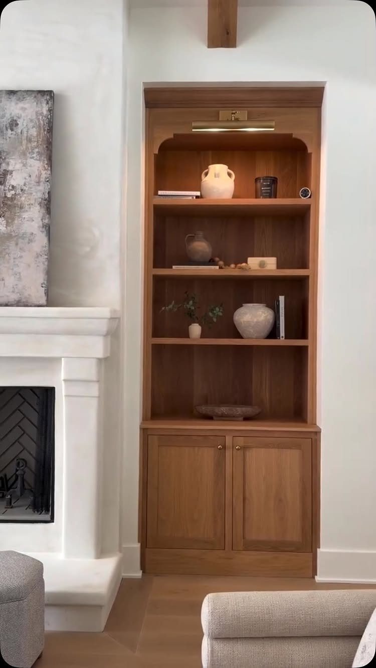 Wooden built-in open shelving unit with decorative vases next to a white fireplace.